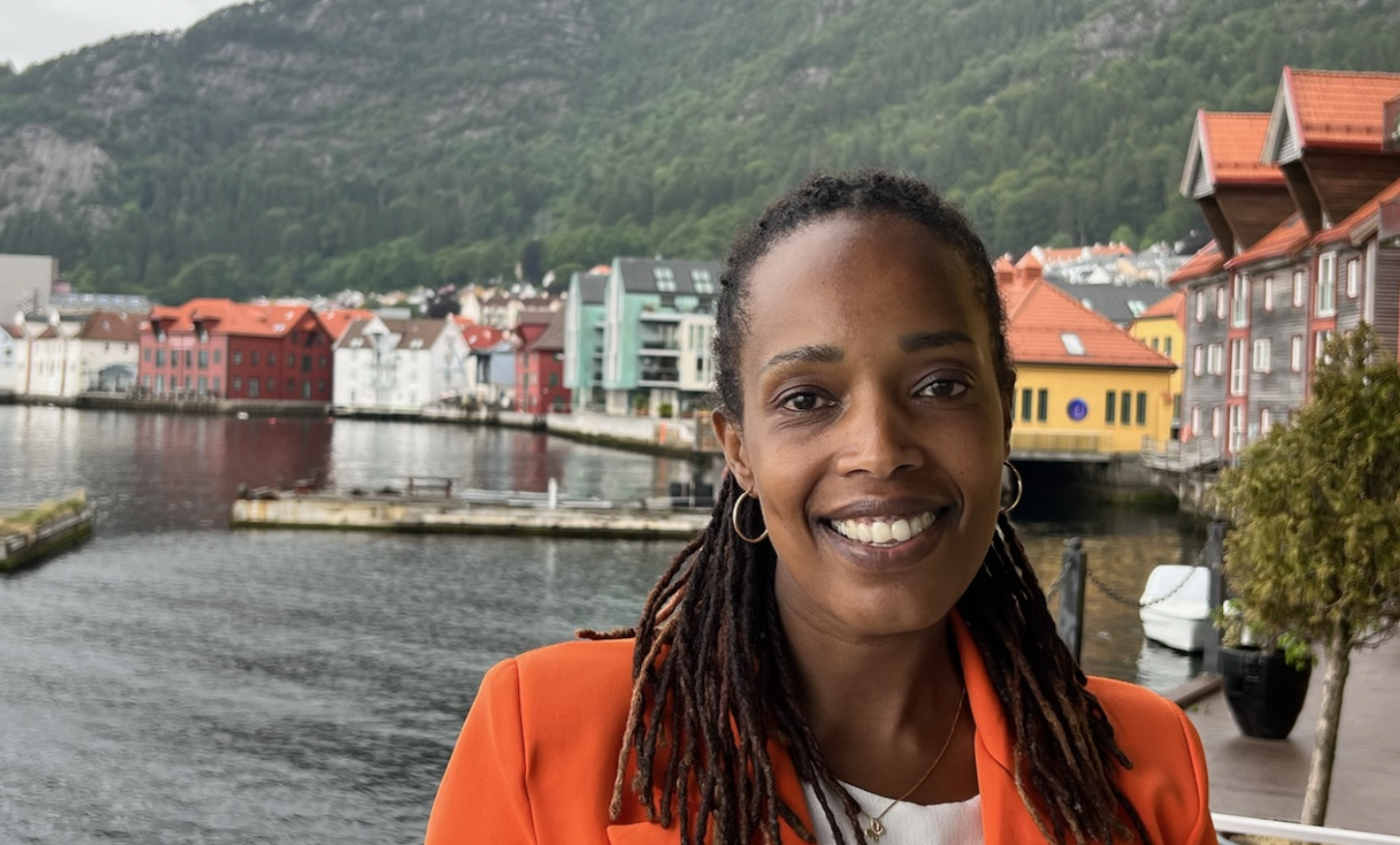 Kvinne (Francine Mbanza Jensen) smiler på brygge i oransje jakke